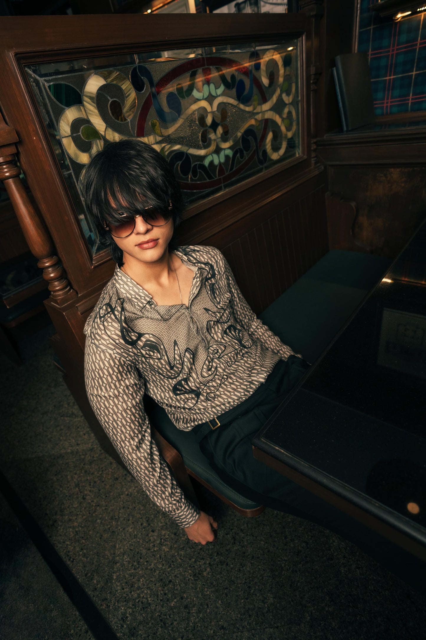 Person wearing a patterned sweater in a dimly lit room with stained glass window