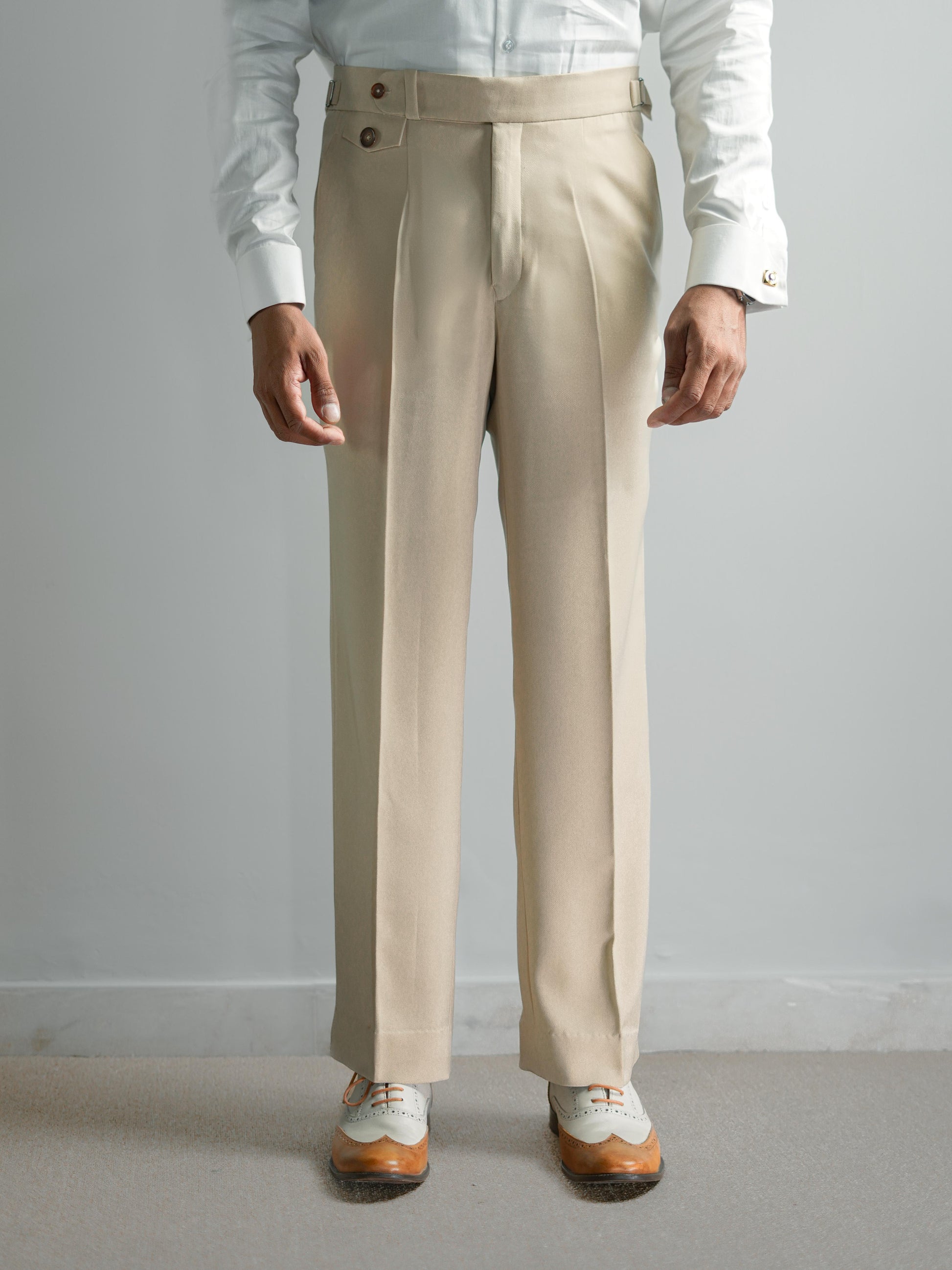 Beige dress pants worn with a white shirt and shoes on a plain background