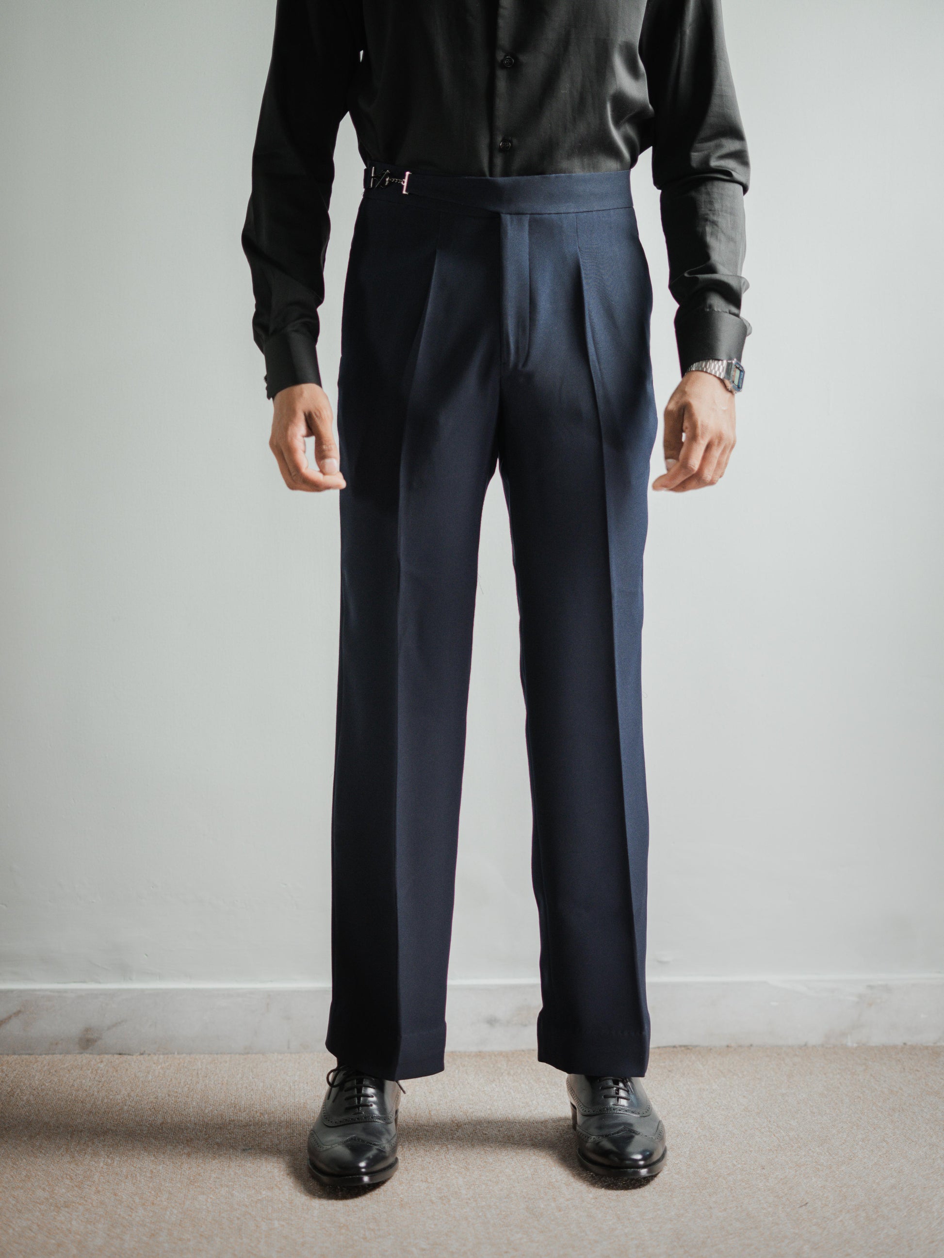 Person wearing navy pleated pants with a plain background