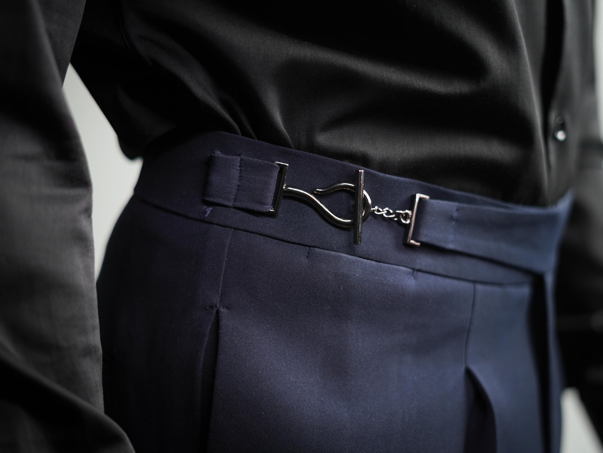 Navy blue pants with a belt featuring a silver buckle on a neutral background