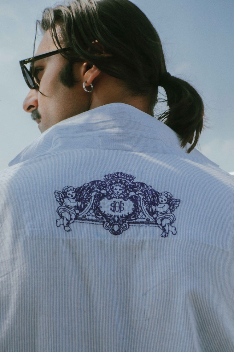 Person wearing a white shirt with an embroidered design on the back, against a clear sky.